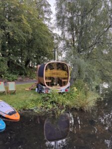 Mobil Hordó Kabin Szauna 88 A TimberIN Nordic Square mobil szauna panorámaüveges hátulnézete utánfutón egy tó mellett